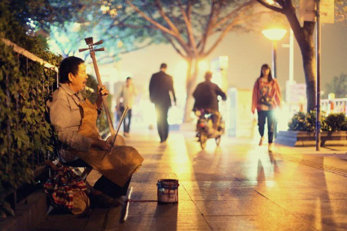 A street musician playing a stringed instrument on the city street at night
