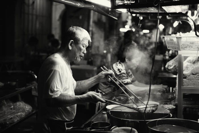 Foto callejera nocturna de un hombre cocinando en un puesto de comida