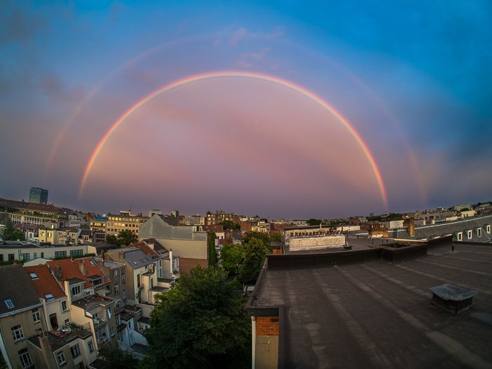 beautiful pink double rainbow against a bright blue sky over an urban rooftop cityscape