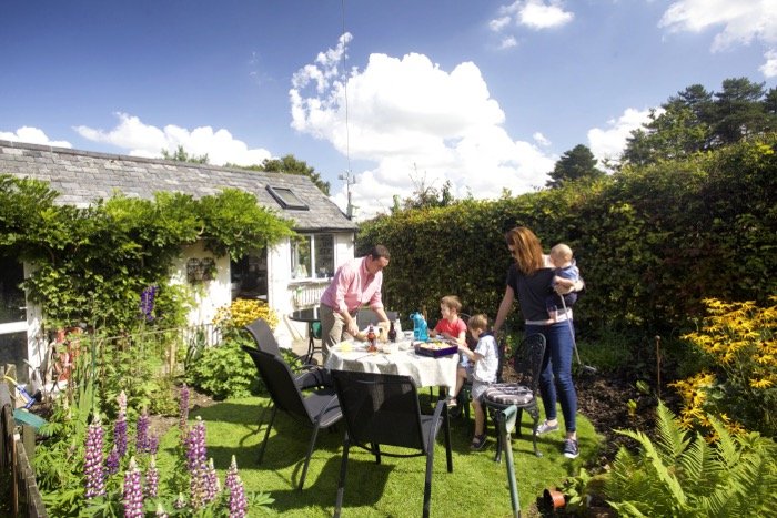 Family eating dinner outdoors in a small sunny garden with flowers