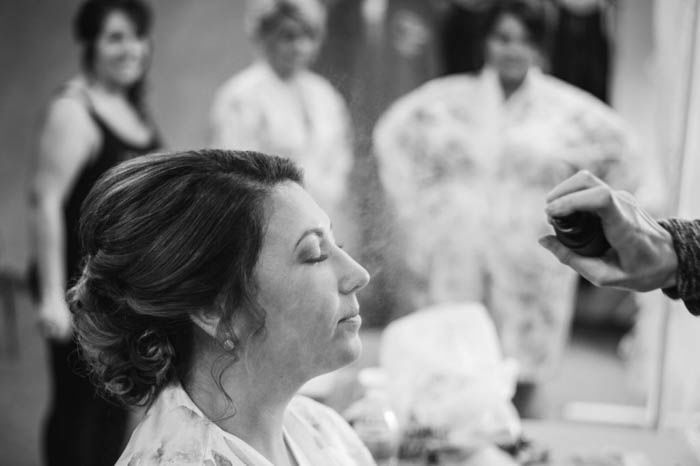 black and white wedding photo of bride getting her makeup done with bridesmaids in the background