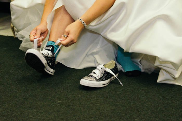 details photo of a bride tying up the shoelaces of her converse shoes under her wedding dress