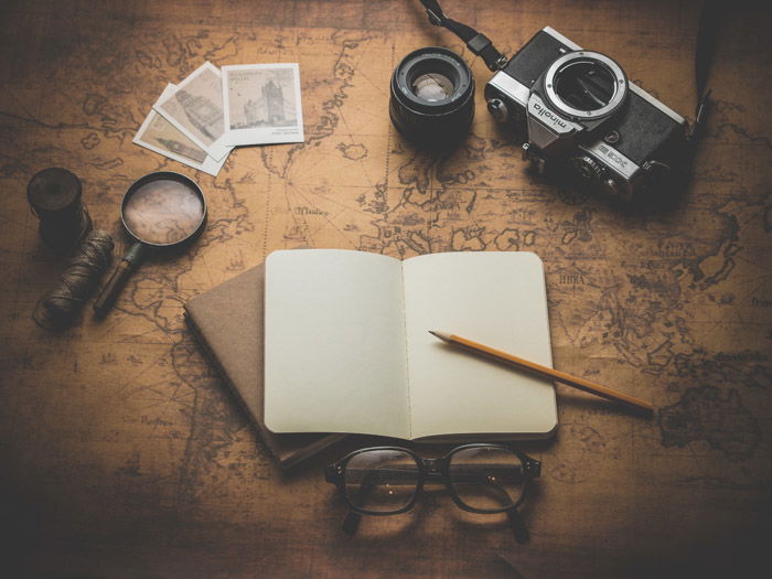 a flay lay of a camera, journals, glasses, and items against a world map