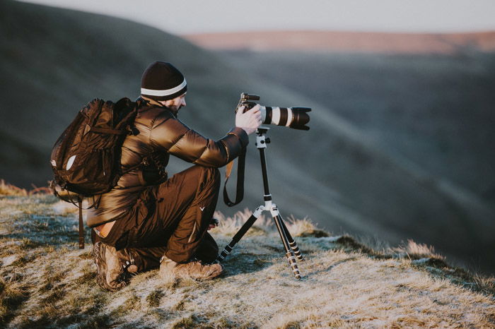 an image of a man in the mountains setting a camera with telephoto lens on a tripod