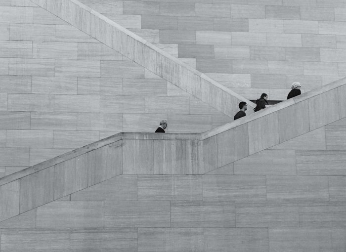 Greyscale photo of people walking up stone stairs
