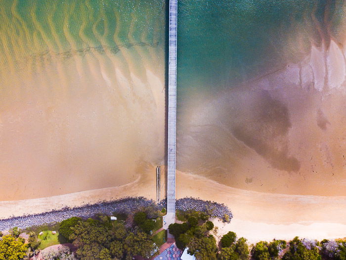 straight down drone photography of a long wooden bridge in shallow water capturing symmetry by combining natural and man-made features