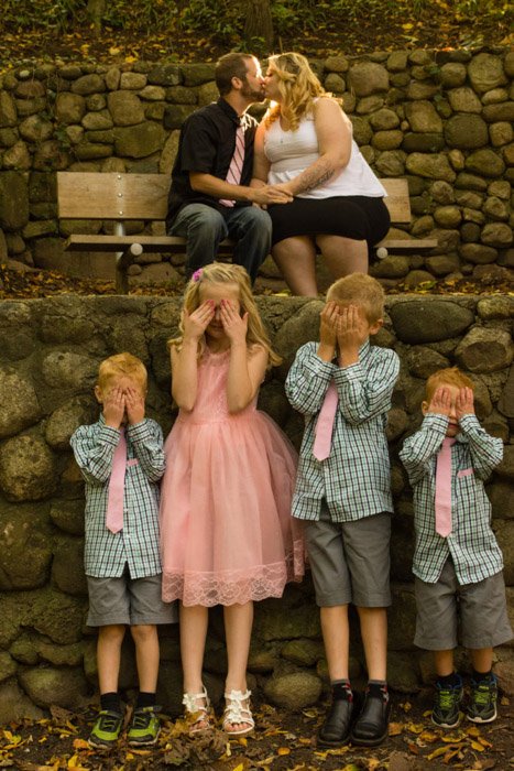 这是一张全家福，四个孩子用手挡住父母的眼睛，在身后接吻