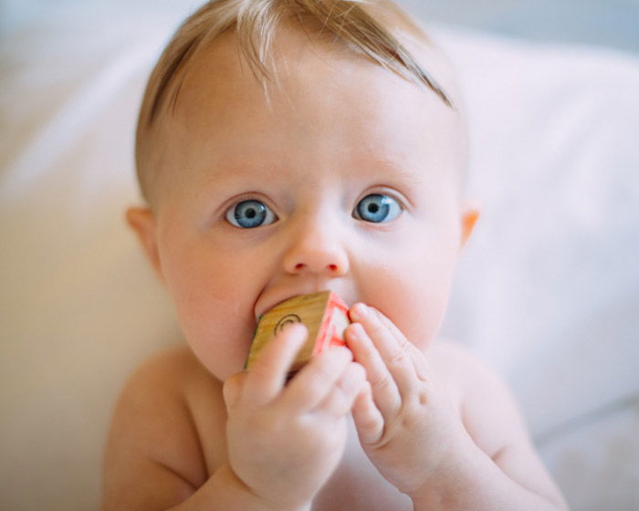 Fotografia recém-nascida de um bebê mastigando um bloco de madeira