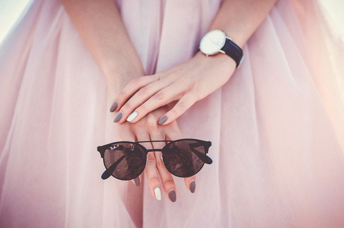 A close up fashion photo of a girl in pink holding sunglasses