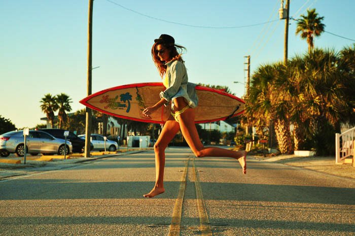 A fashion photography shot of a female model walking with a surfboard