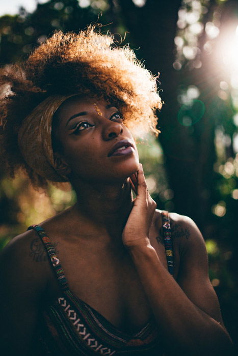 A female model touching her face, standing outside in the sunshine