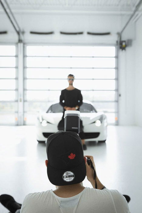 A man taking a portrait of a male model standing in front of a car