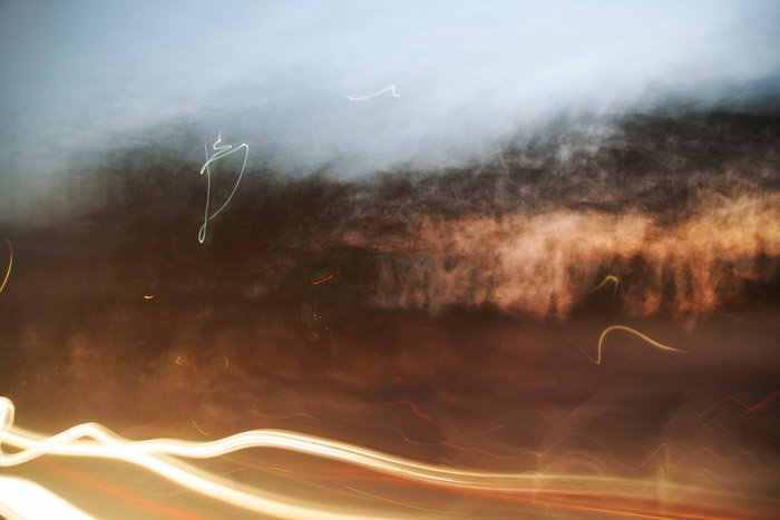 Slow-shutter photograph of blurry light trails and bushes. taken while travelling a highway at dusk. Abstract photography ideas.