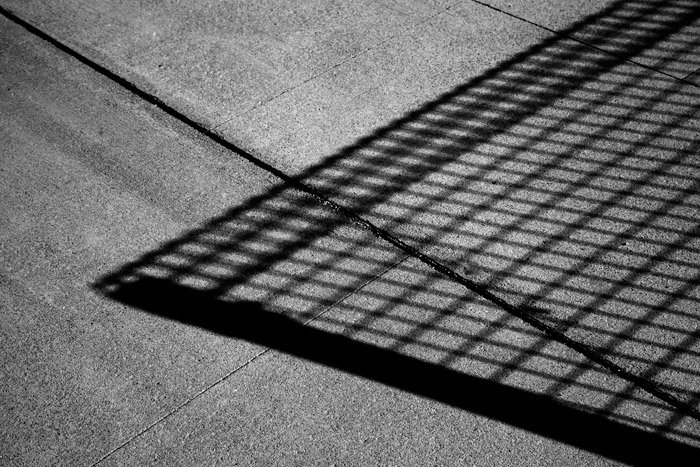 Black and white photography of the shadow of a wire mesh fence on concrete. Abstract photography ideas.
