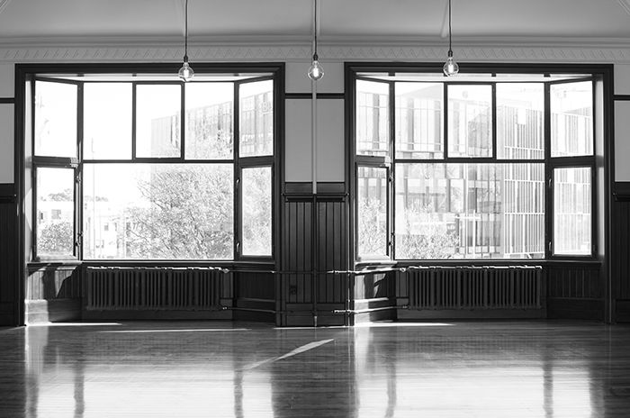 Black and white photograph of a large empty room with 2 big french windows, the restored former billiards room of the Midland Club Building, Christchurch, New Zealand.