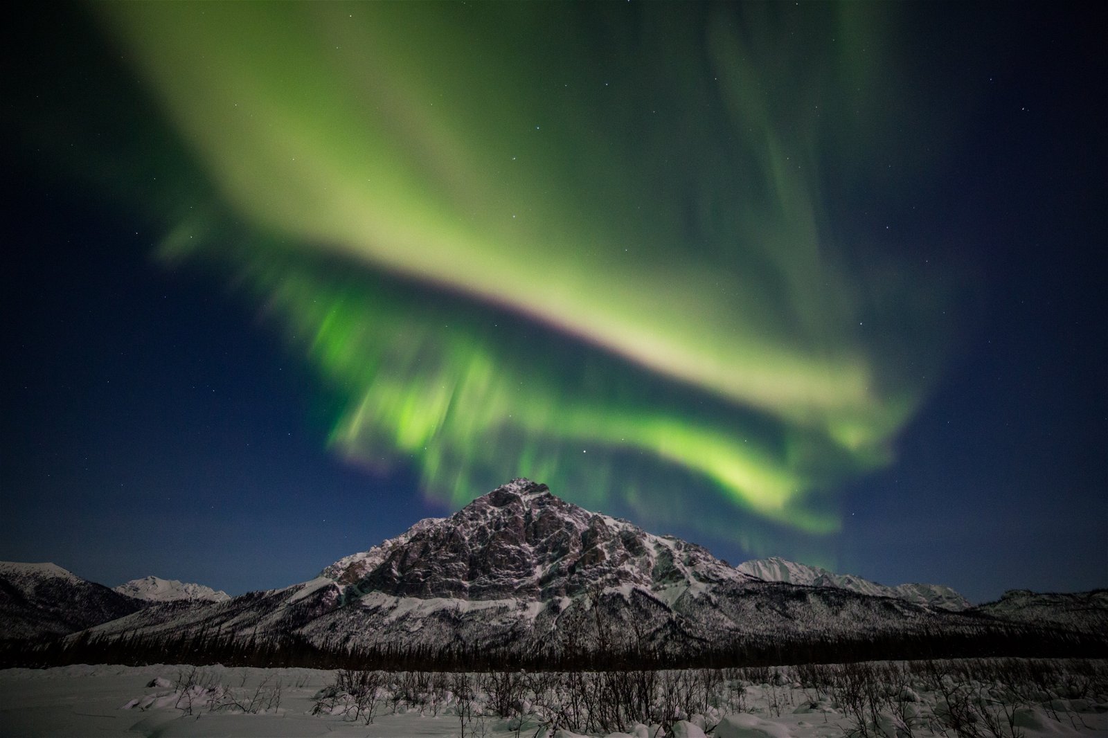 Bright green northern lights above a snowy. mountain and landscape