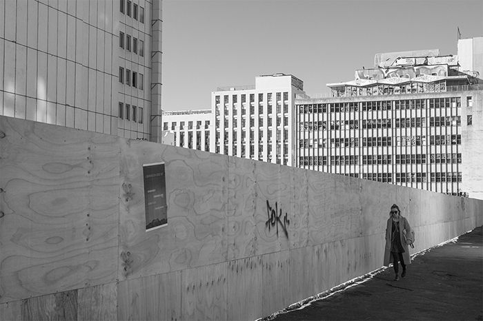 Black and white street photo of a city worker walking past an empty building site.. Creative street photography