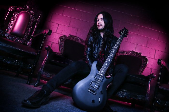 Moody gothic style portrait of a man in black holding a black electric guitar, sitting on Gothic style furniture with purple light and shadows behind. Improve your photography skills today. 