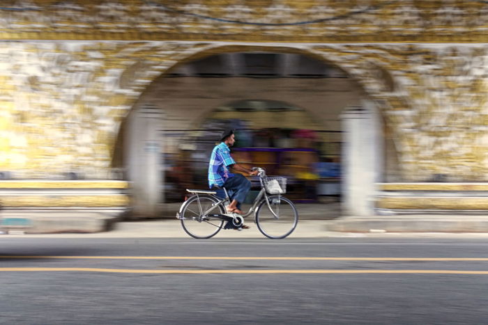 Street photography of a man riding a bicycle with blurry background.