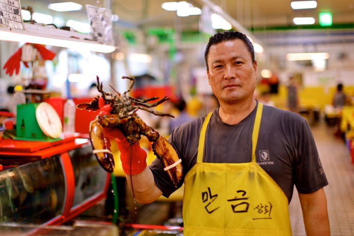 Portrait of a man in a fish market holding a lobster.