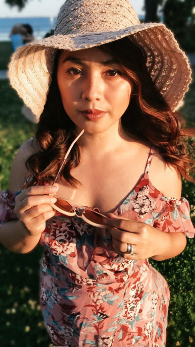 Portrait of a girl in pink flowery dress and straw hat looking at the camera, holding her sunglasses on a bright day - Smartphone fashion photography shoot