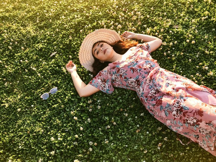 Girl in pink flowery dress and straw hat lying back on the grass on a bright day - Smartphone fashion photography shoot