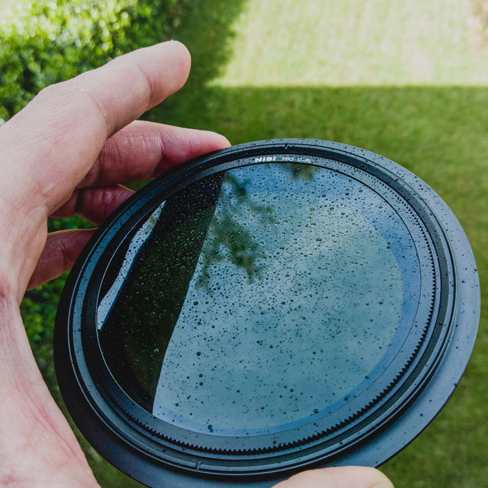 Close up of a hand holding a rain splattered camera lens filter 