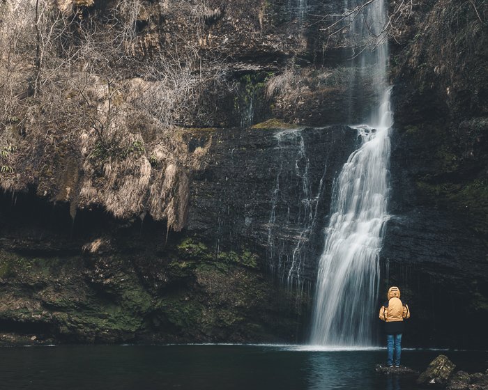 Photo of a person in yellow standing in front of a waterfall.