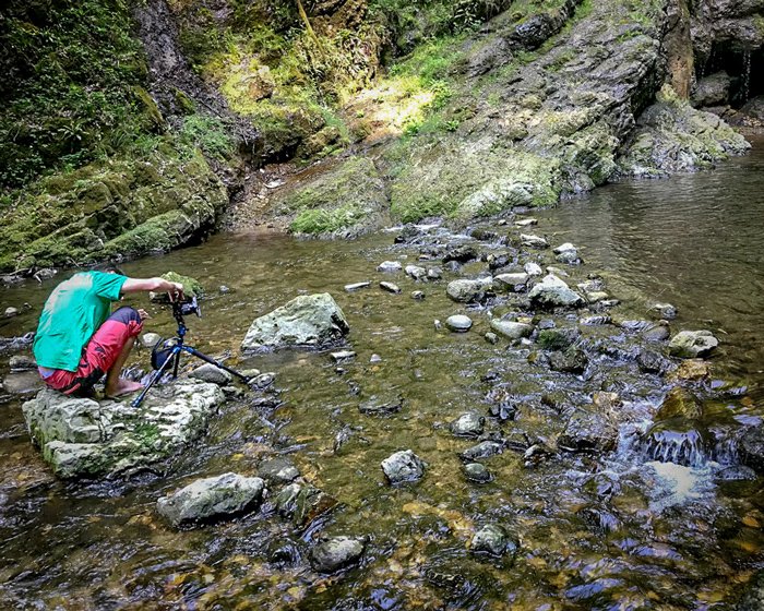 A photographer sitting on a rock with tripod and camera to take waterfall images