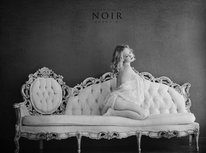 Black and white photo of a girl kneeling on a white chaise longue