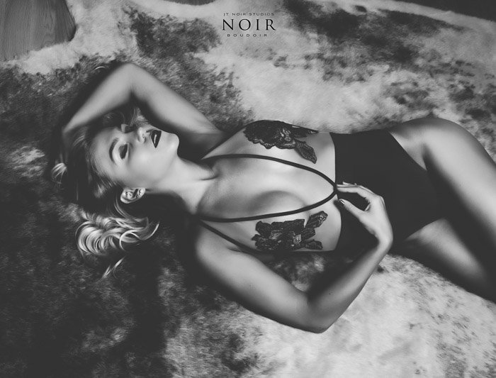 Black and white boudoir photo of a blonde girl in black and white lingerie lying on her back