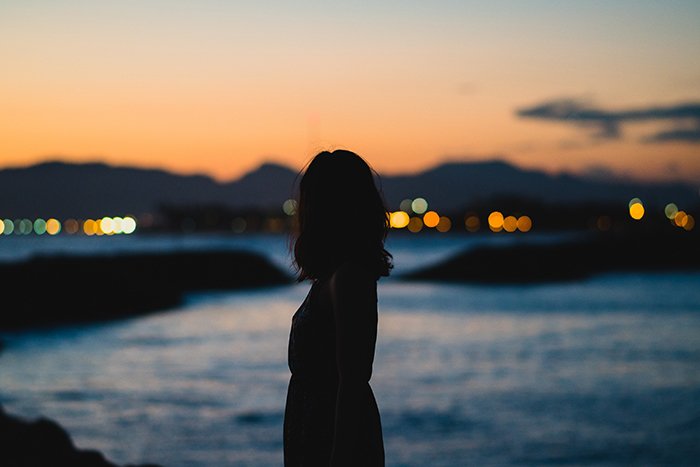 一个女人的剪影站在傍晚海景的前景-无脸肖像摄影