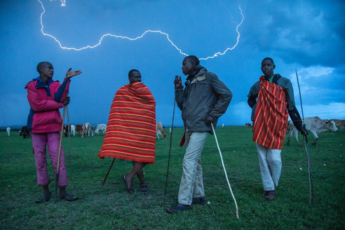 Night photography of 4 African men standing outdoors with lightning striking in the background