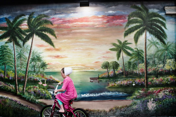 Photo of a girl riding a bike past a painted landscape by Dina Litovsky. Famous photographers to follow. 