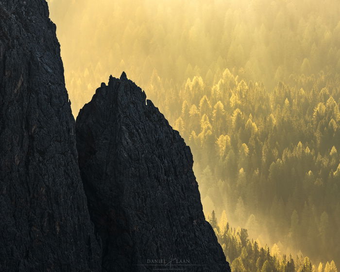 A fine art landscape photography shot of a rocky mountain in front of a brilliant yellow and green forest.