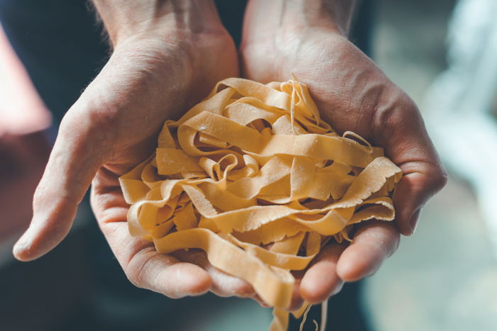 Food photography of hands holding fresh pasta. 