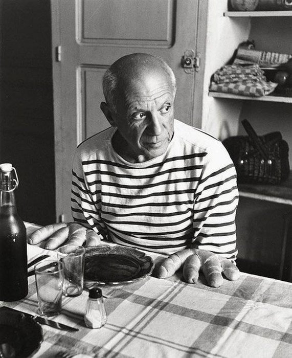 Robert Doisneau black and white photograph of Pablo Picasso sitting at a table posed as if bread were his hands 