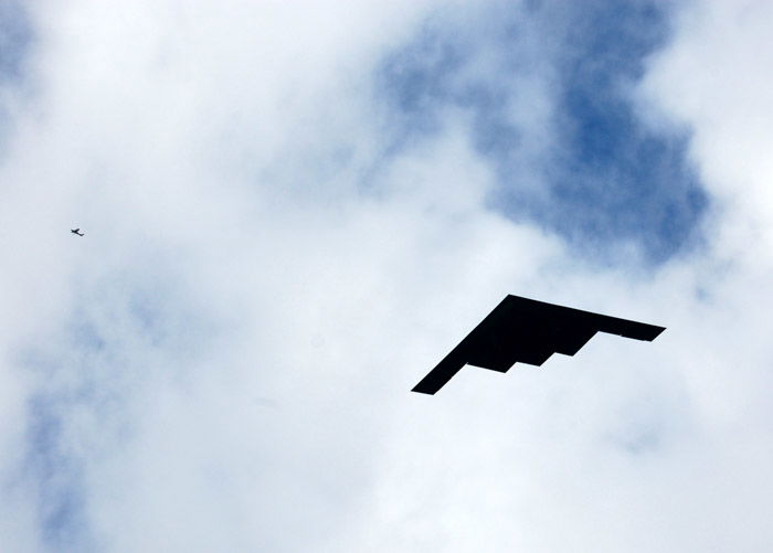 Photograph of the sky with an airplane juxtaposed to a paper airplane. 