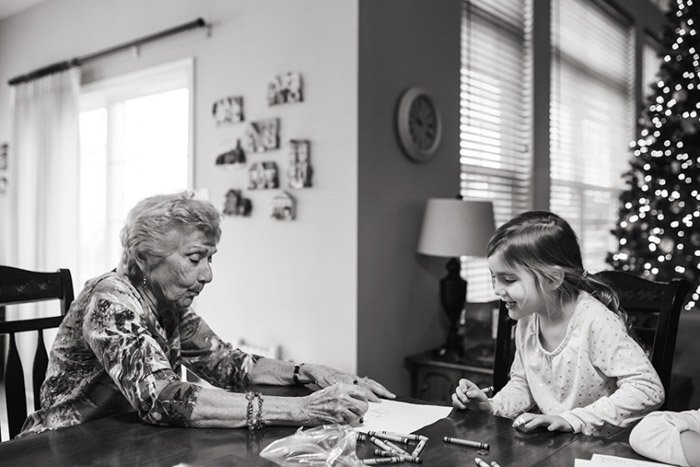 Black and white photograph of a grandmother and child at a table colouring in a book