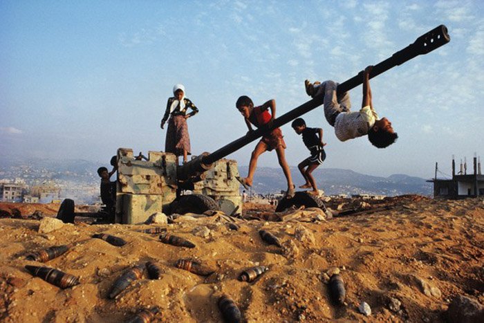 Documentary photography of children playing around a disused and abandoned artillery weapon.