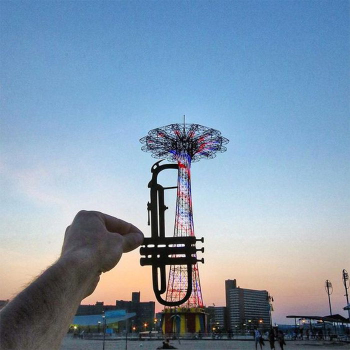 Photo of the photographer extending his afront of the lens wrm and placing a cutout version of a trumpet in hile photographing 