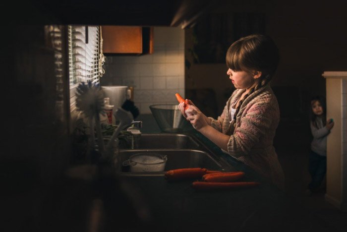 A photo of a little girl peeling carrots at the kitchen sink