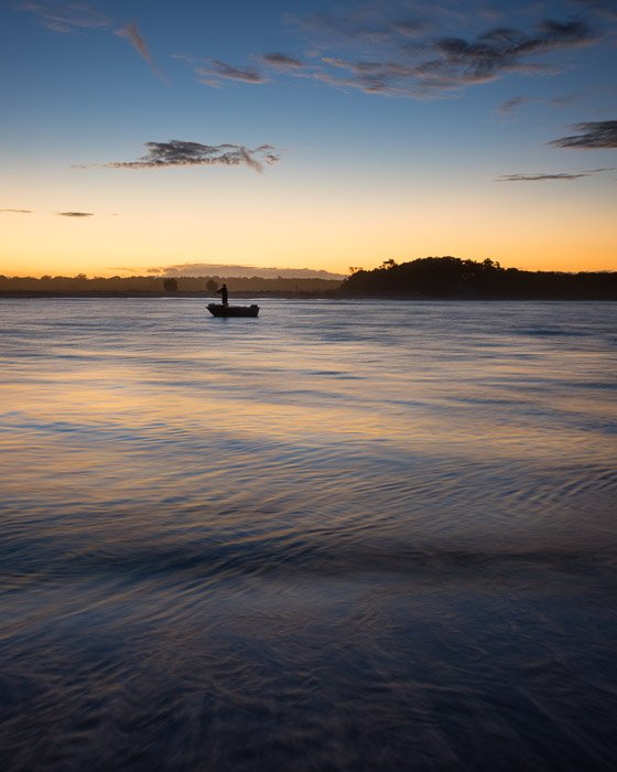 A figure in a small boat on water at evening. Landscape photography composition