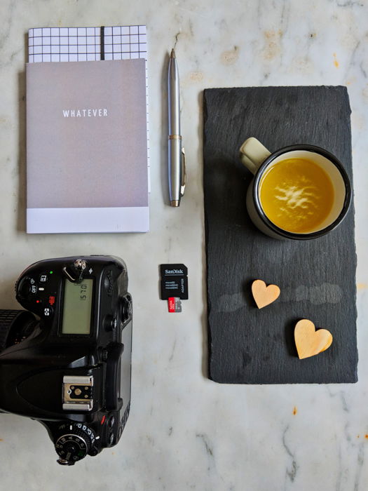 Overhead still life photography shot of a camera, notebook, pen, coffee cup and memory card