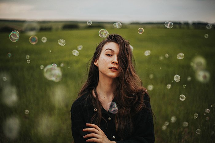 natural light portrait of a girl standing in green fields surrounded by bubbles