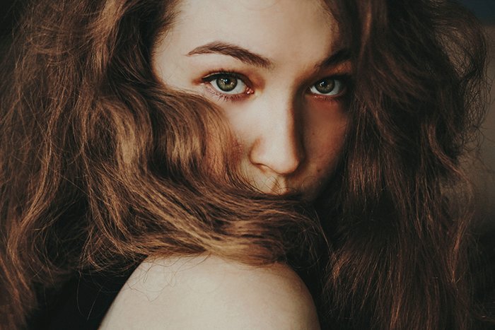 close up portrait of a girl looking across her shoulder into the camera, hair swept across her face and focus on her eyes, natural light portrait photography