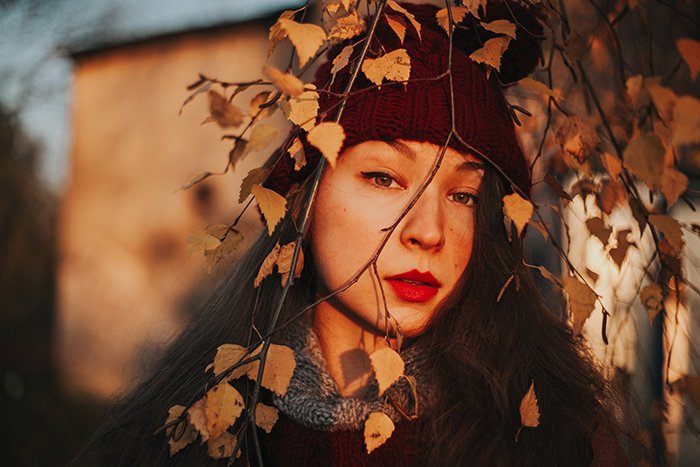 natural light portrait of girl in red hat looking out through autumn trees