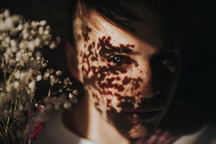 shadowy close up of a girls face, a bunch of flowers casting dreamy shadows on her face. Natural light portrait photography