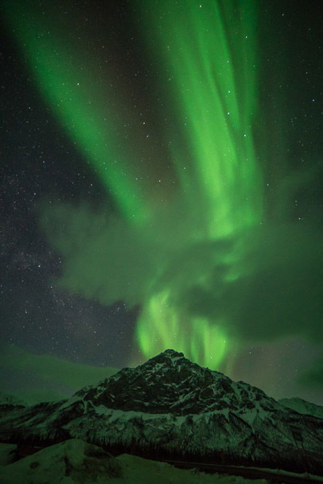 Photograph of the northern lights in Alaska with an icy mountain in the foreground