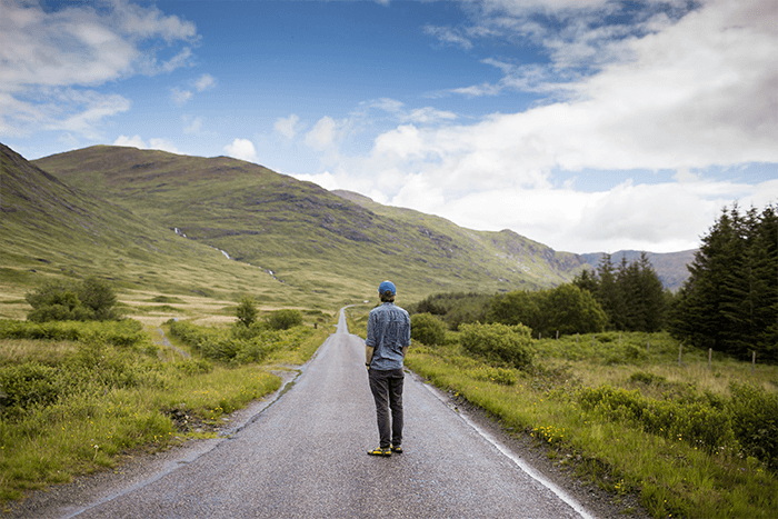 a man standing in the middle of a road among a green landscape